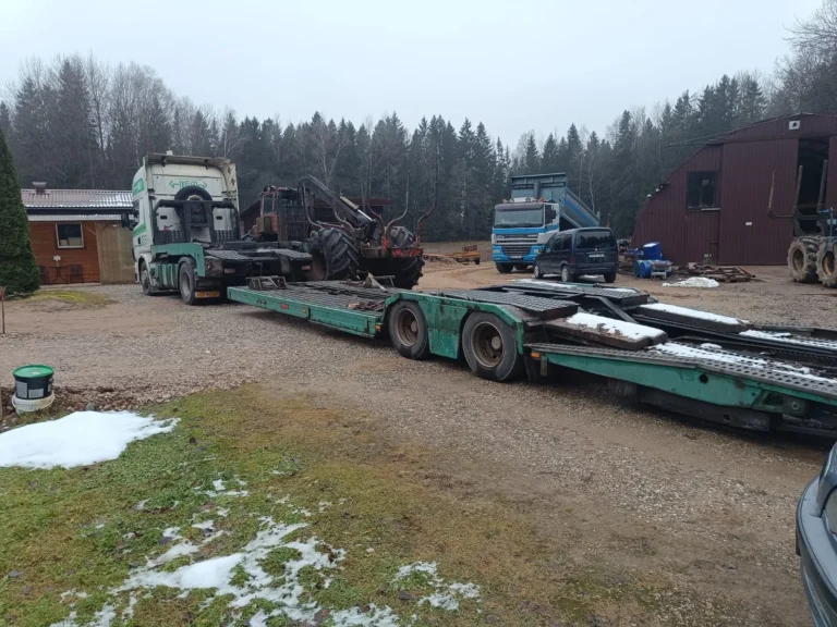 green and white metal truck with flatbed trailer and ramp, parked near